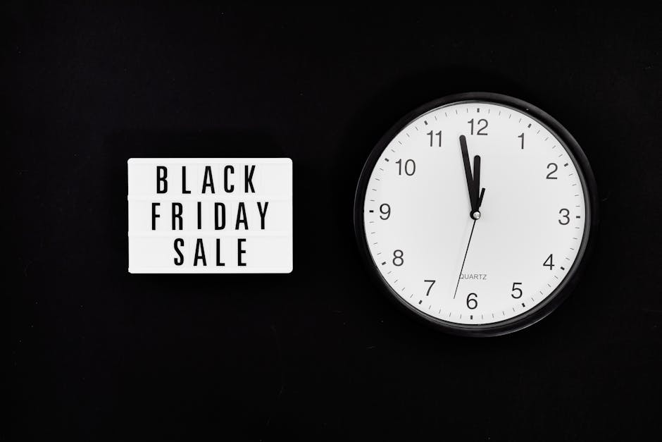 A black background featuring a white rectangular sign with bold black lettering reading 'BLACK FRIDAY SALE' positioned to the left, and a round white quartz clock with black numerals and hands showing